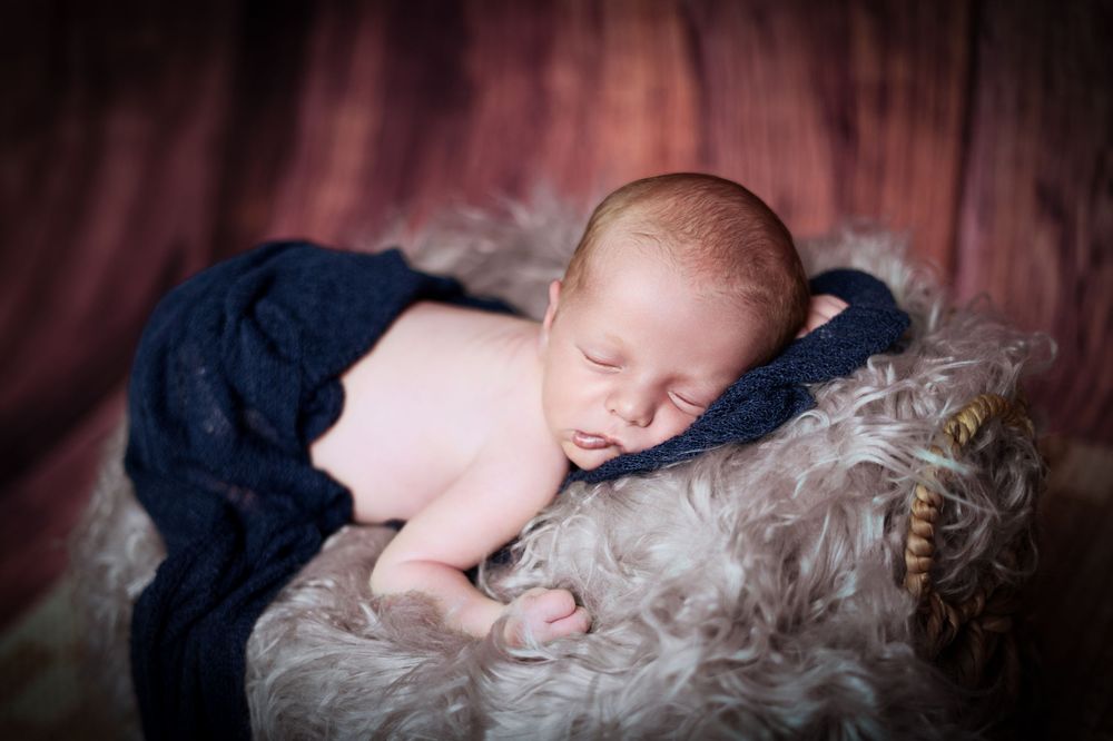 Sleeping newborn in navy outfit on textured gray fur backdrop.
