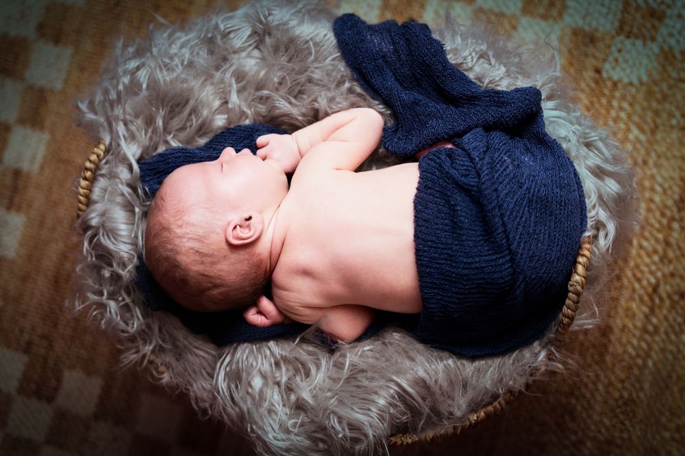 Newborn wearing dark blue outfit resting on fluffy gray fur surface.