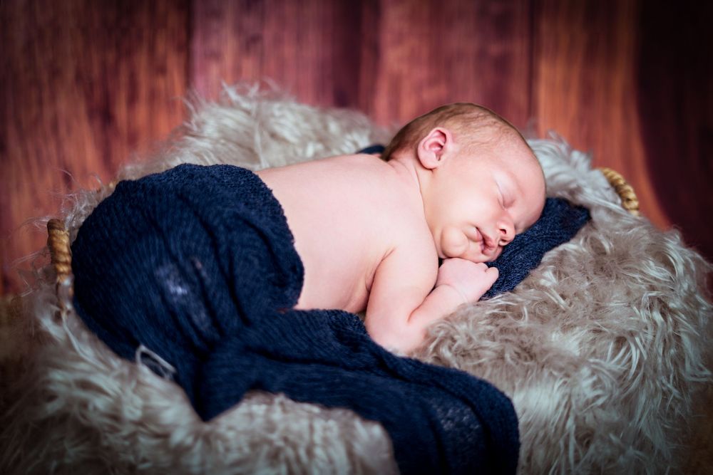 Sleeping baby in navy outfit on soft gray fur blanket.