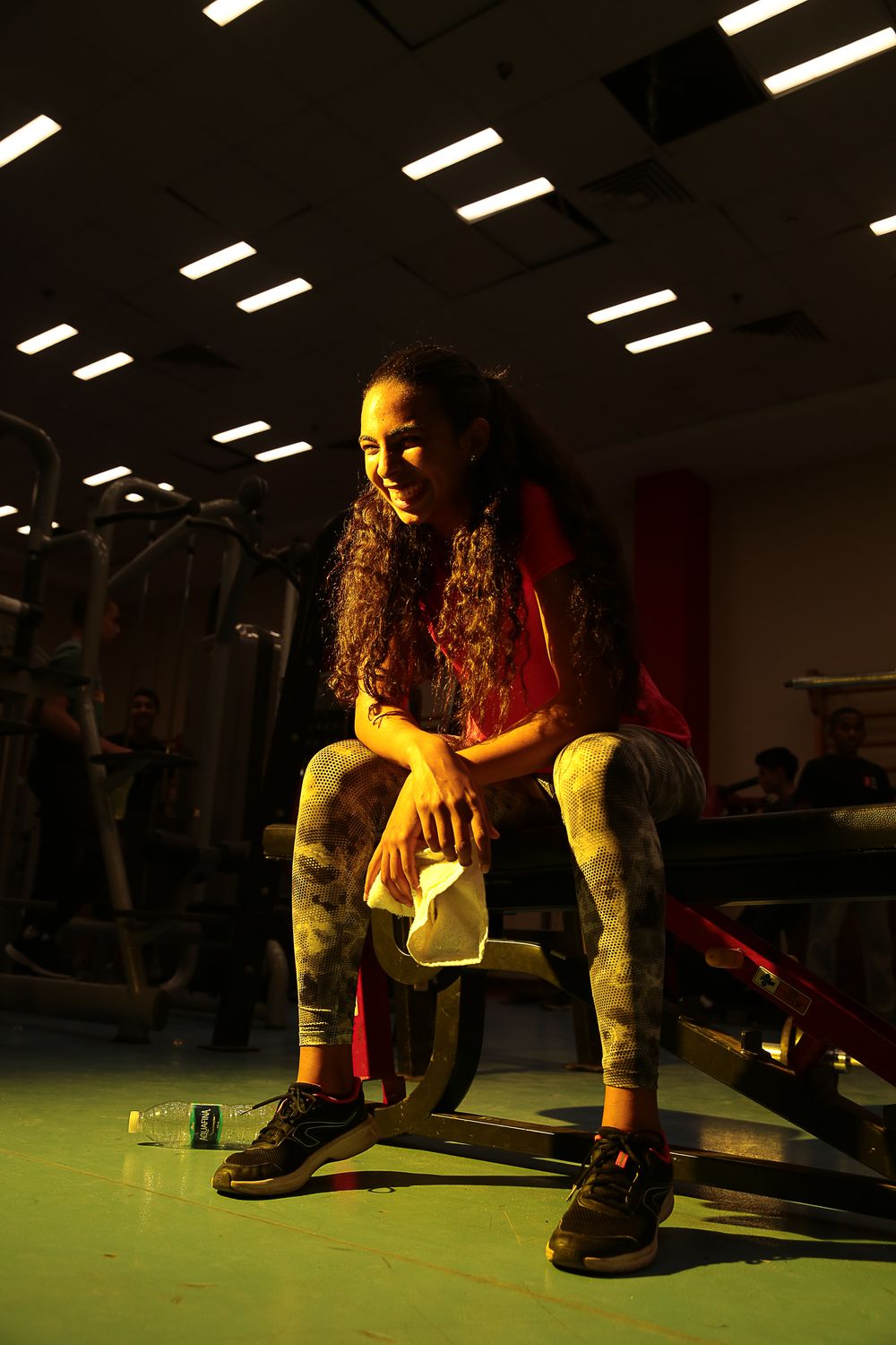Person in workout gear stretches on gym floor under dramatic lighting.