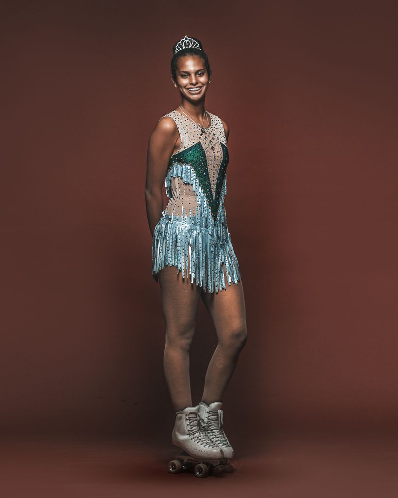 Roller skater wearing sparkly blue costume with fringe and tiara poses against brown background.