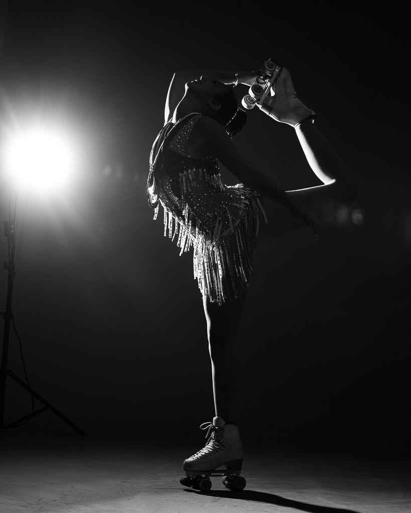 Figure in fringed costume performing artistic roller skating move in dramatic lighting.