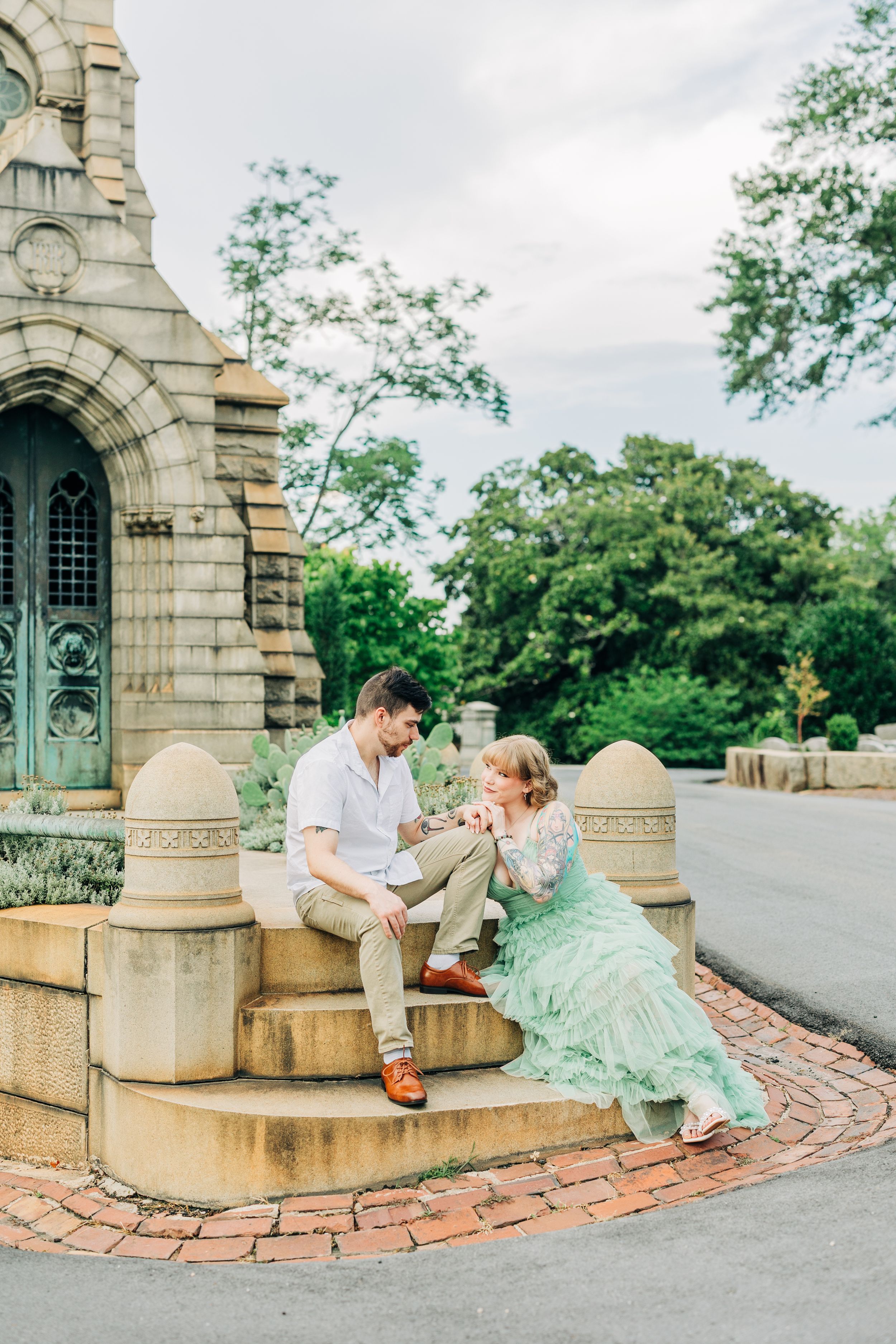 Couple in romantic photo session posed along curved brick wall and stone archway at sunset.