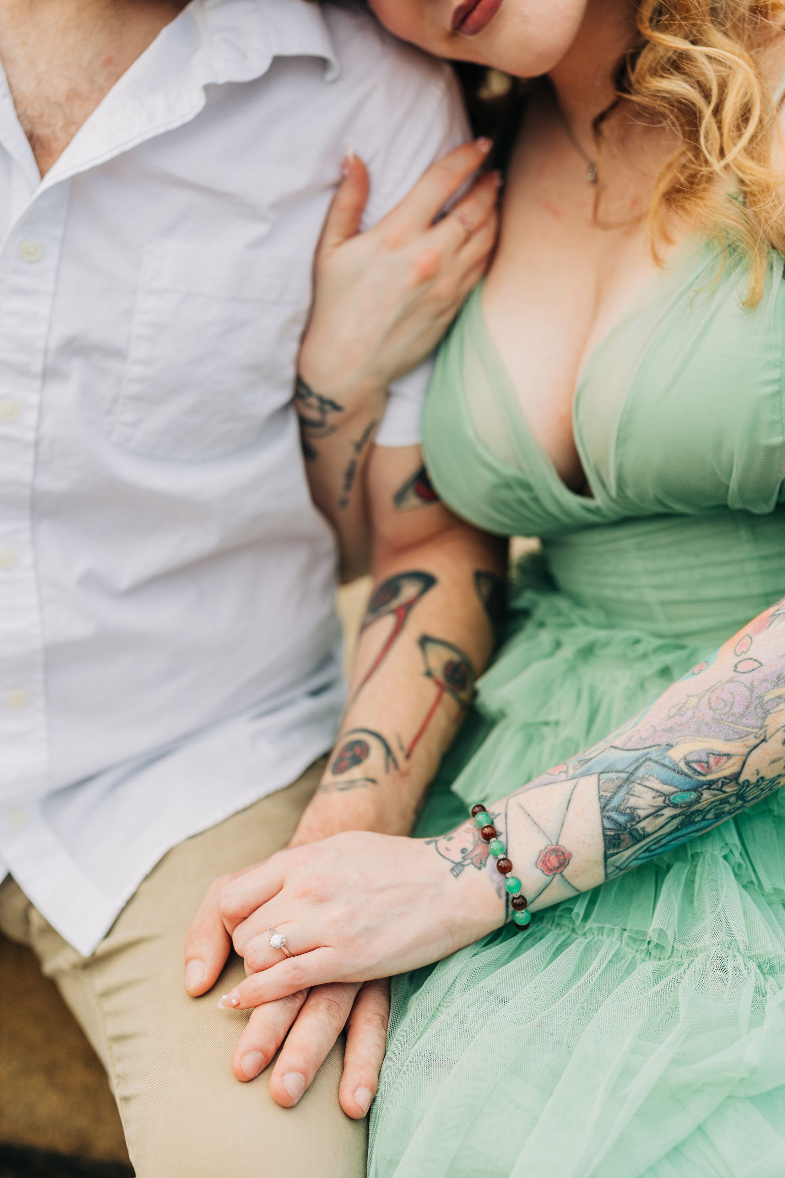 Close up of couple holding hands, showing intricate arm tattoos and mint green dress details in romantic pose.