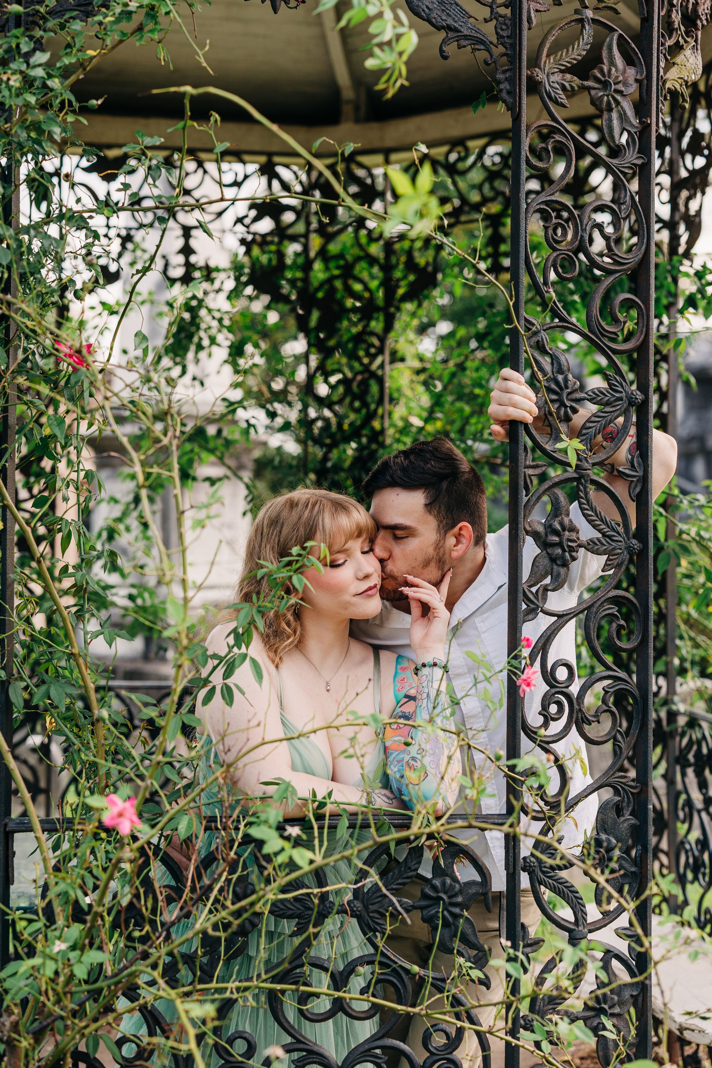 Romantic couple sharing an intimate moment in an ornate garden gazebo with wrought iron details and climbing vines.