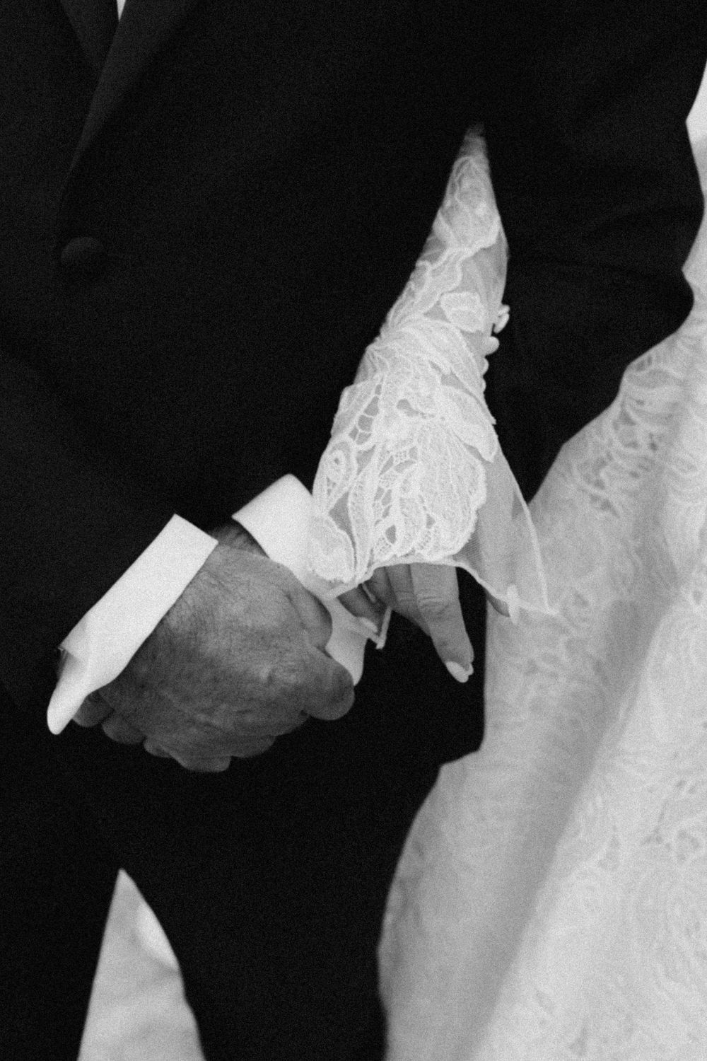 Black and white close-up shows couple in formal wedding attire gently holding hands during a romantic moment.