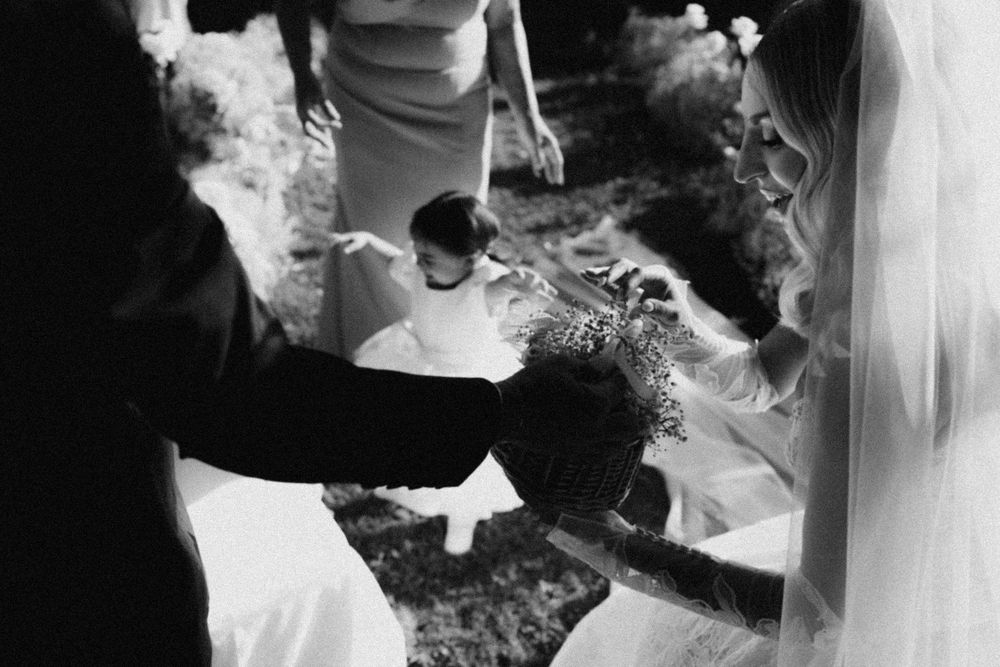 Black and white photograph showing hands holding flower petals outdoors during a ceremonial moment.