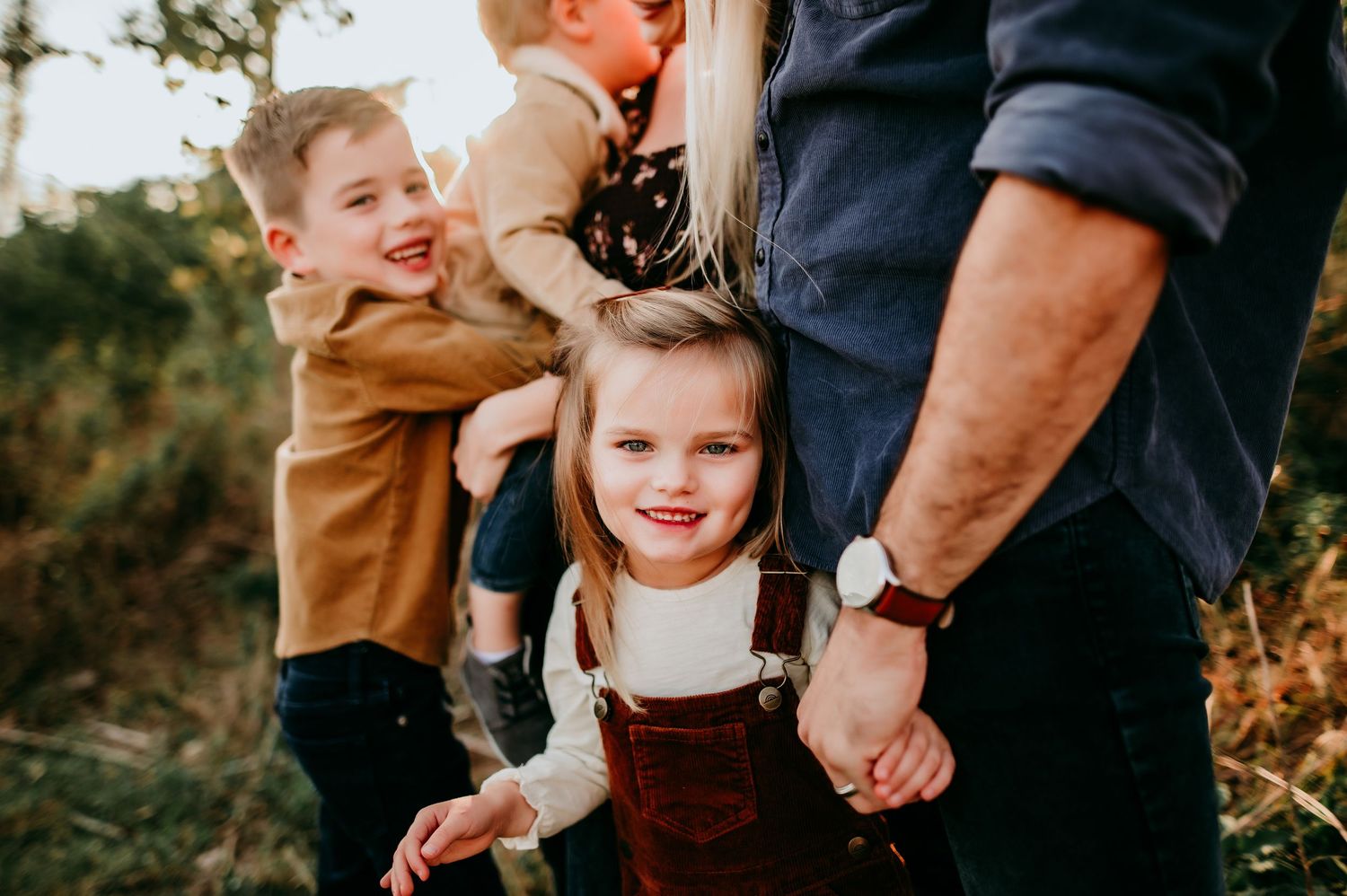 Family holds hands on nature walk at sunset creating candid lifestyle moments during autumn golden hour.