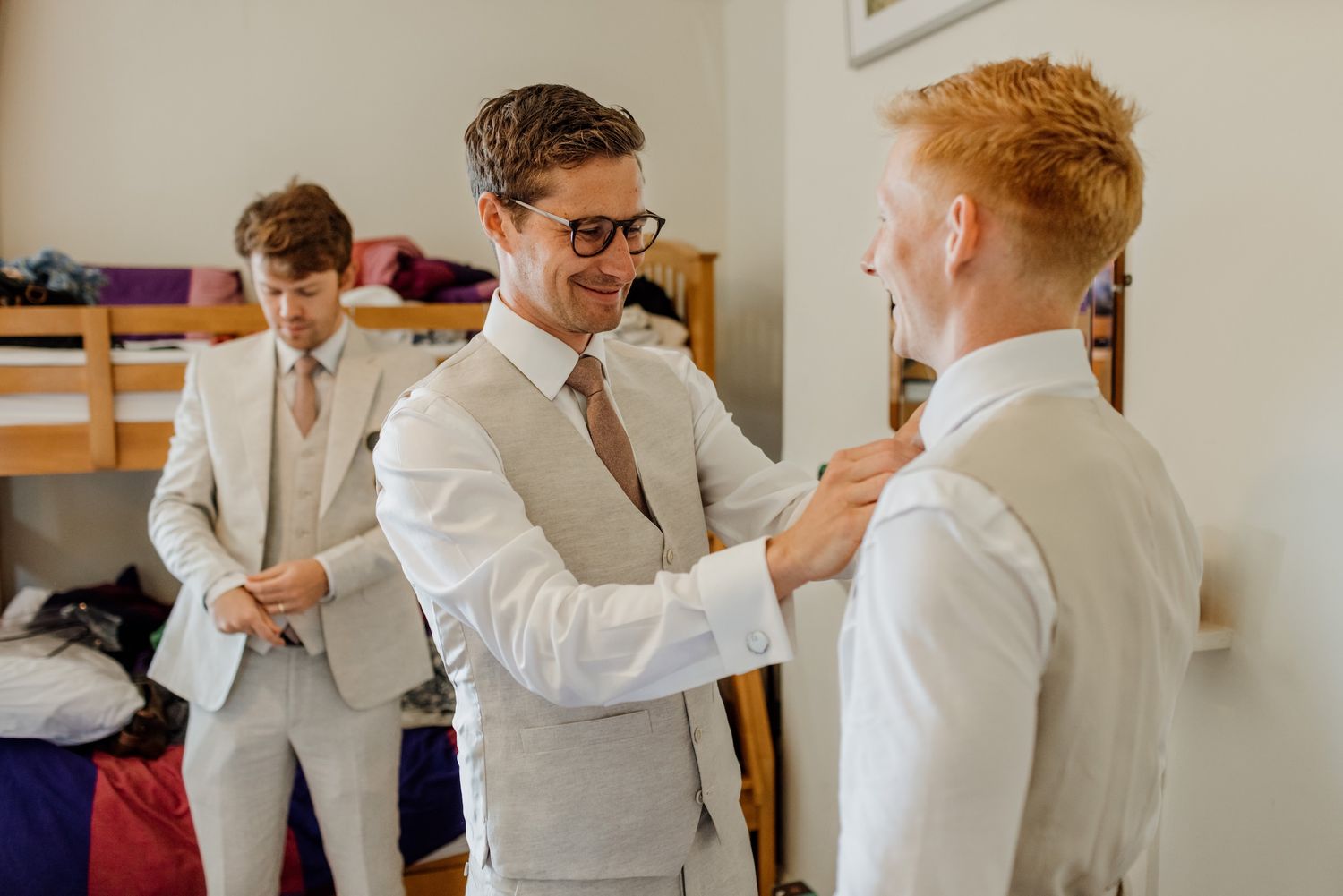 Wedding party preparations with groomsmen helping each other get dressed in white shirts.