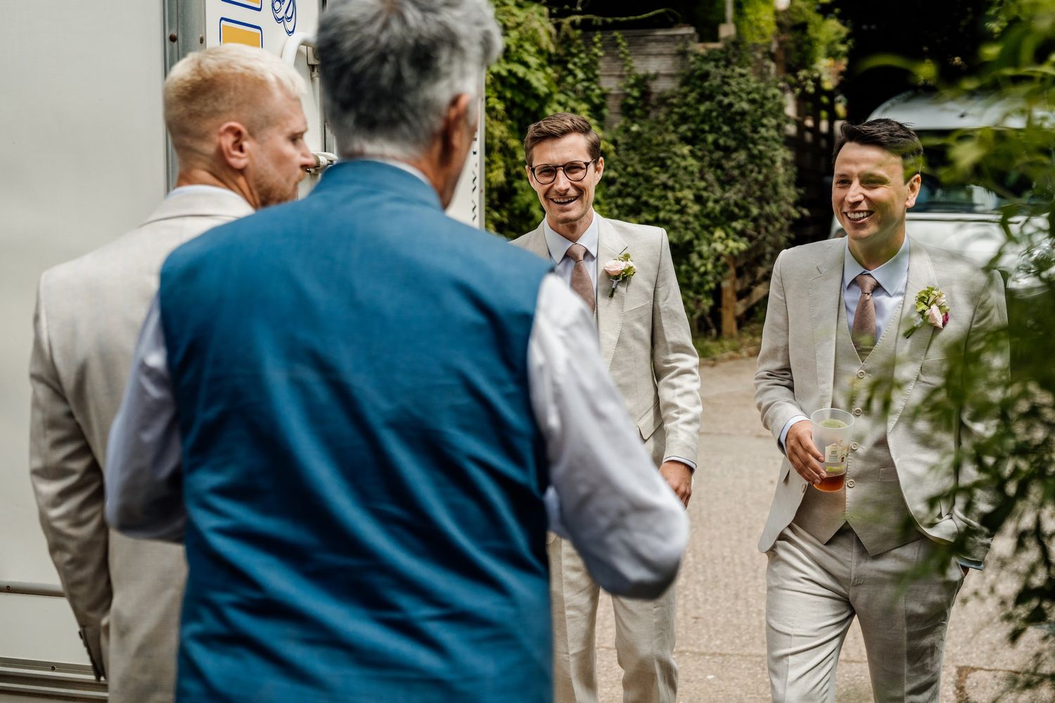 Wedding party in light gray suits laughing together outdoors.