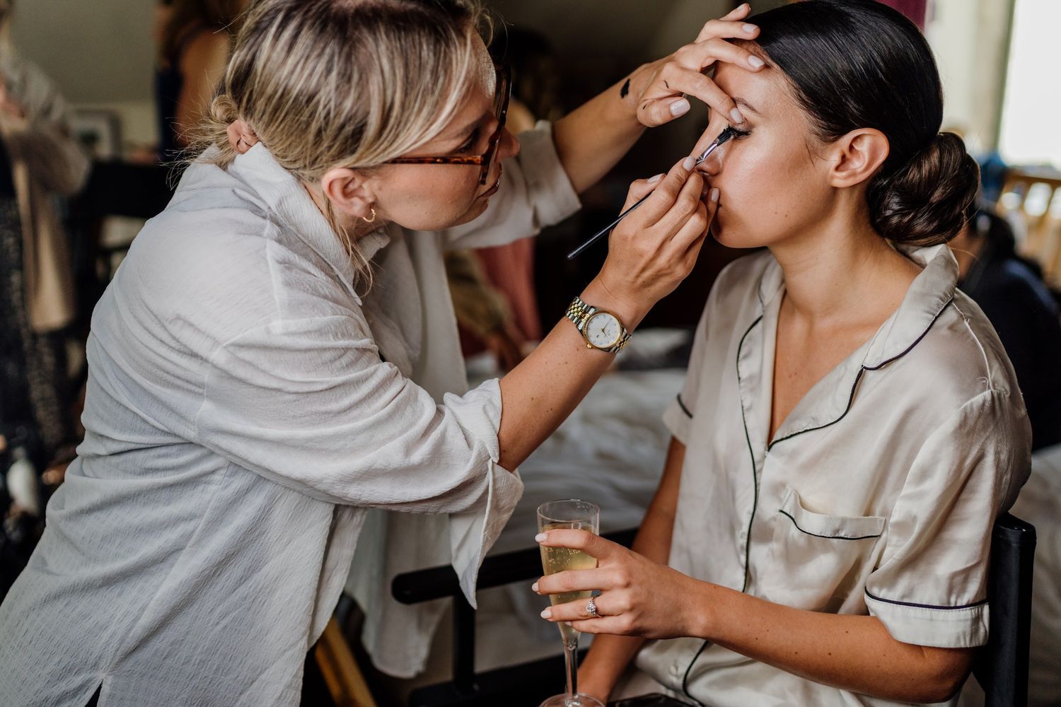 Wedding party getting ready with professional makeup application in a brightly lit room.