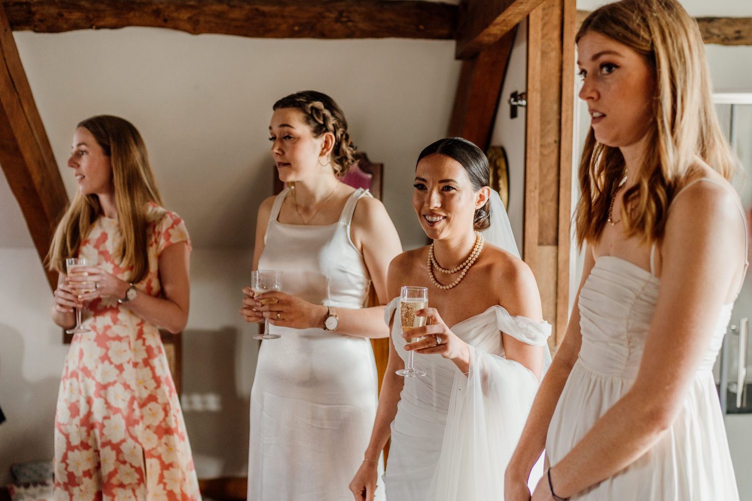 Women in white and floral dresses gather in a bright indoor space during wedding preparations.