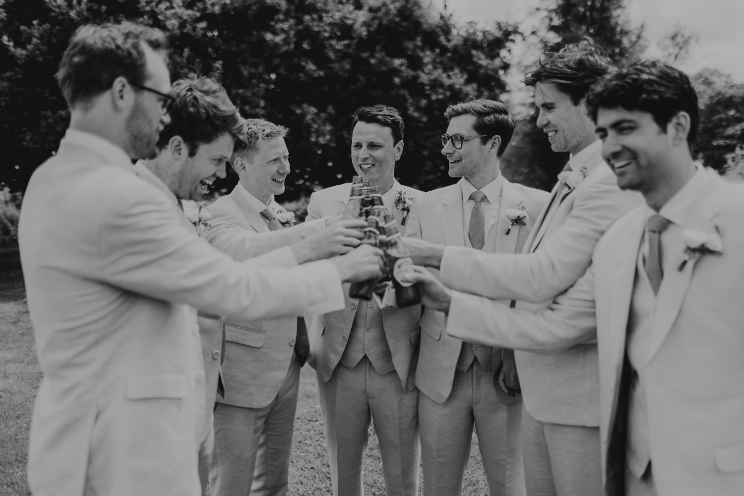 Joyful groomsmen in light gray suits share candid laughs together outdoors.