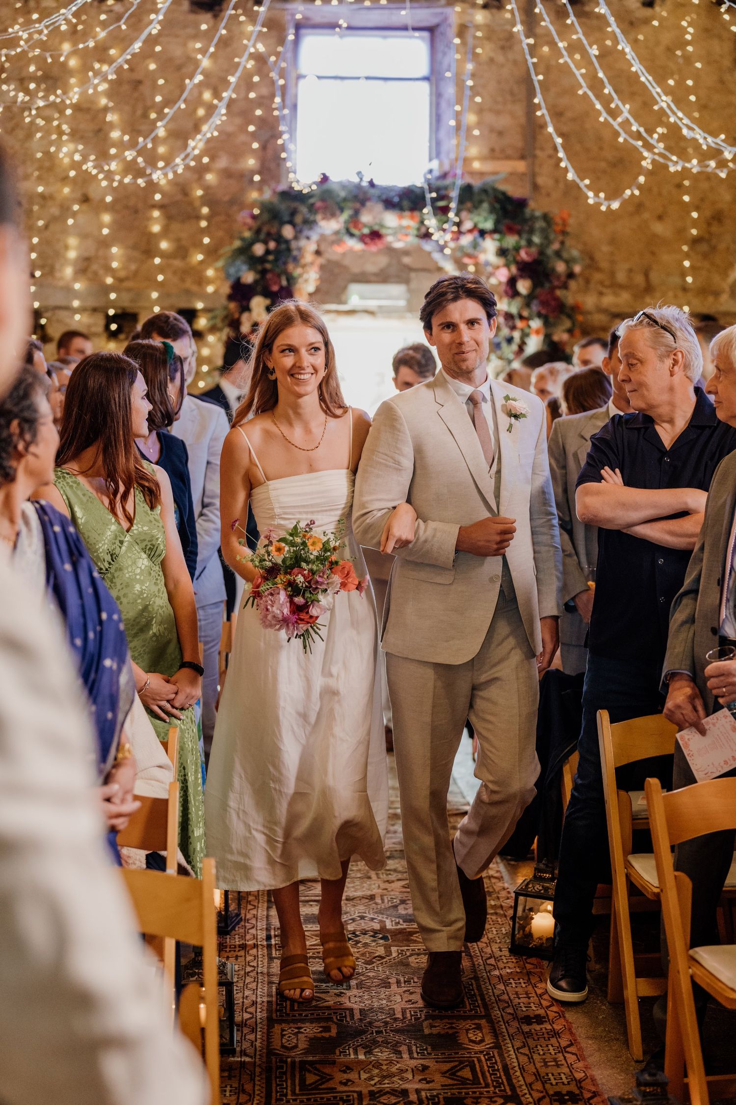 Indoor wedding reception with string lights and guests mingling in a rustic venue.
