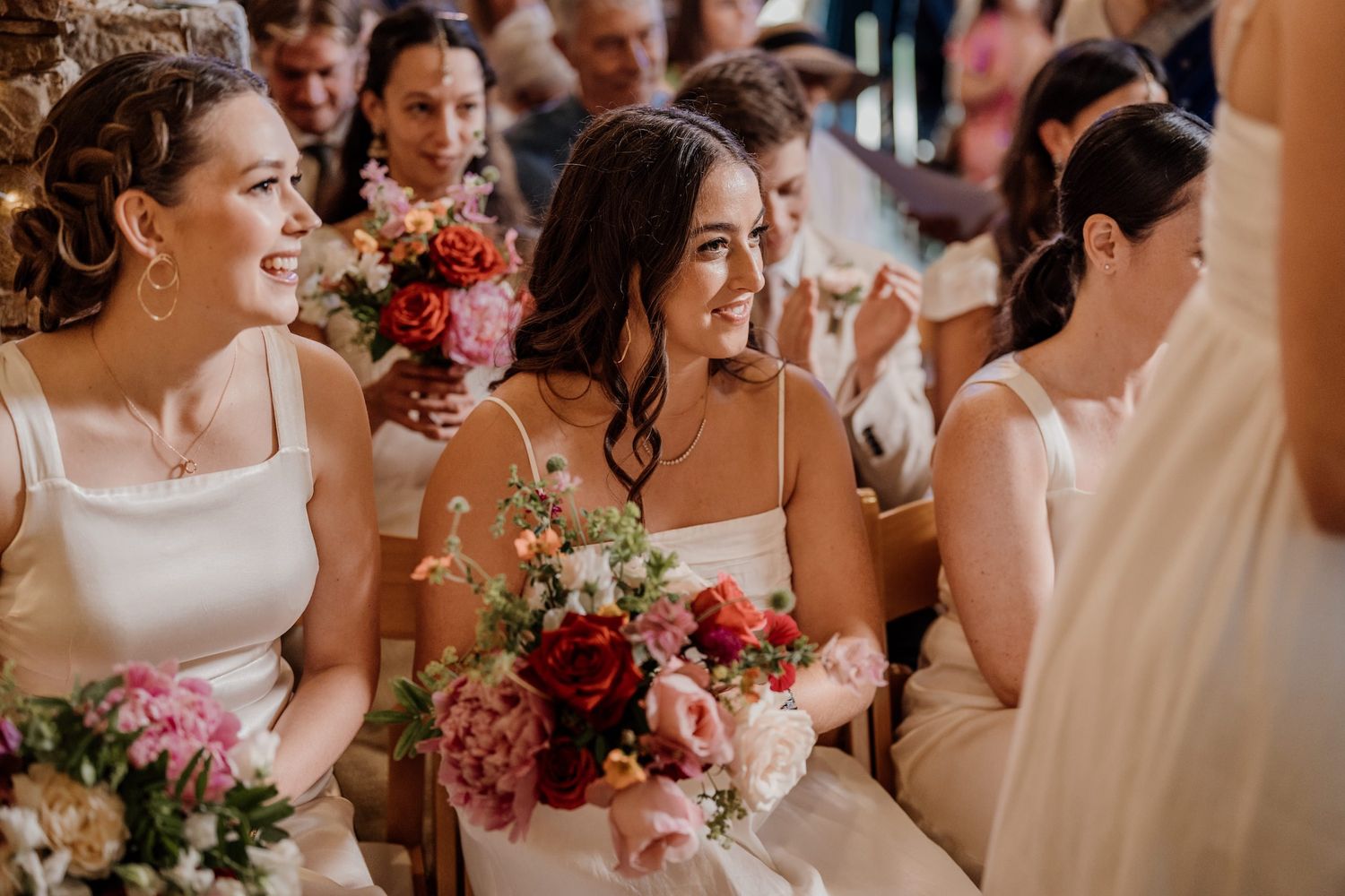 Wedding party dressed in light colors stands together sharing joyful laughter and smiles.