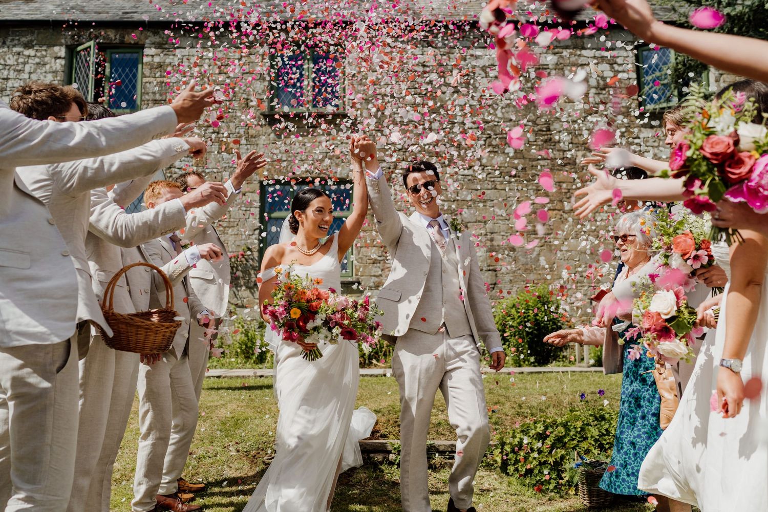 Festive moment with pink confetti being tossed over wedding attendees in white attire outdoors.