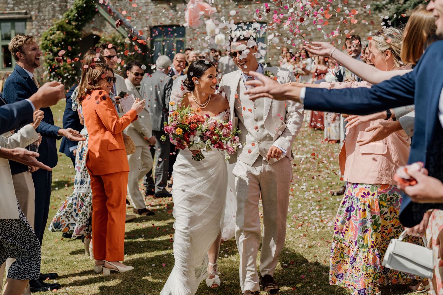 Wedding guests tossing flower petals during outdoor celebration with bright fashion choices.