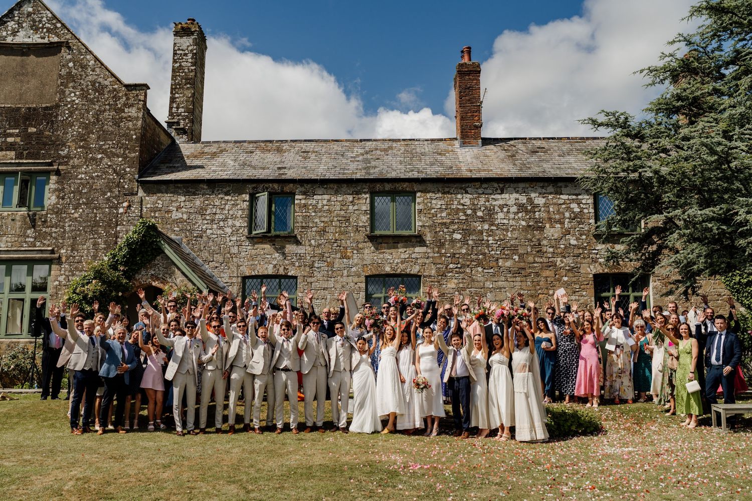 Large group photo of wedding guests gathered outside a historic stone building.