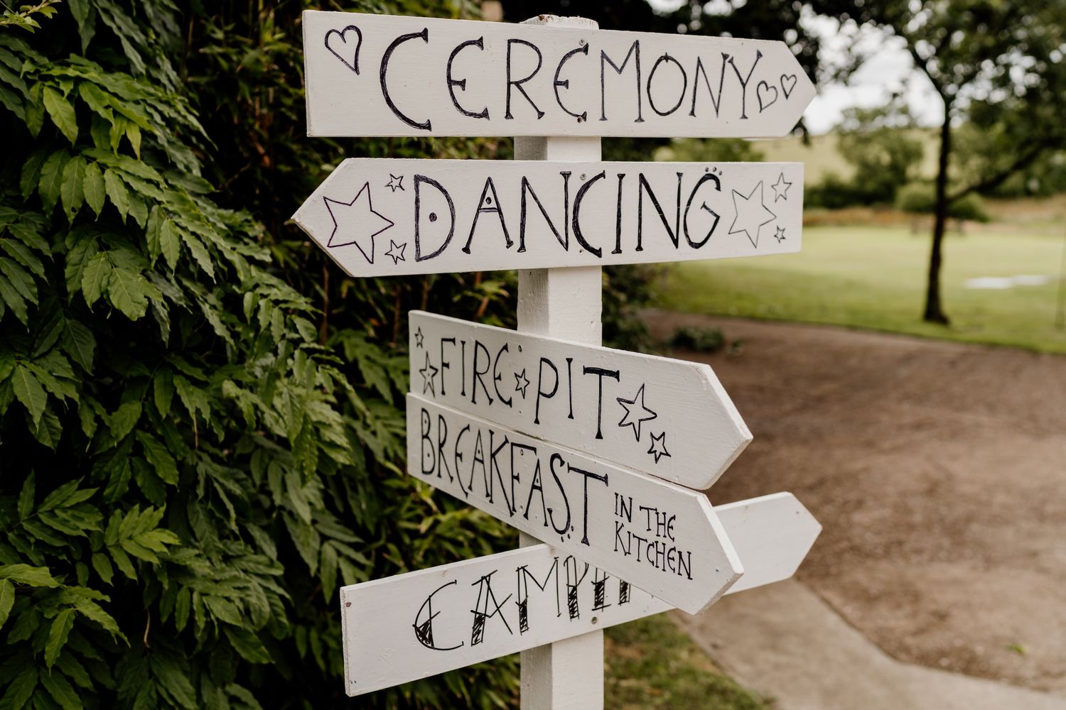Handwritten directional signs for a wedding ceremony and reception posted in a garden setting.