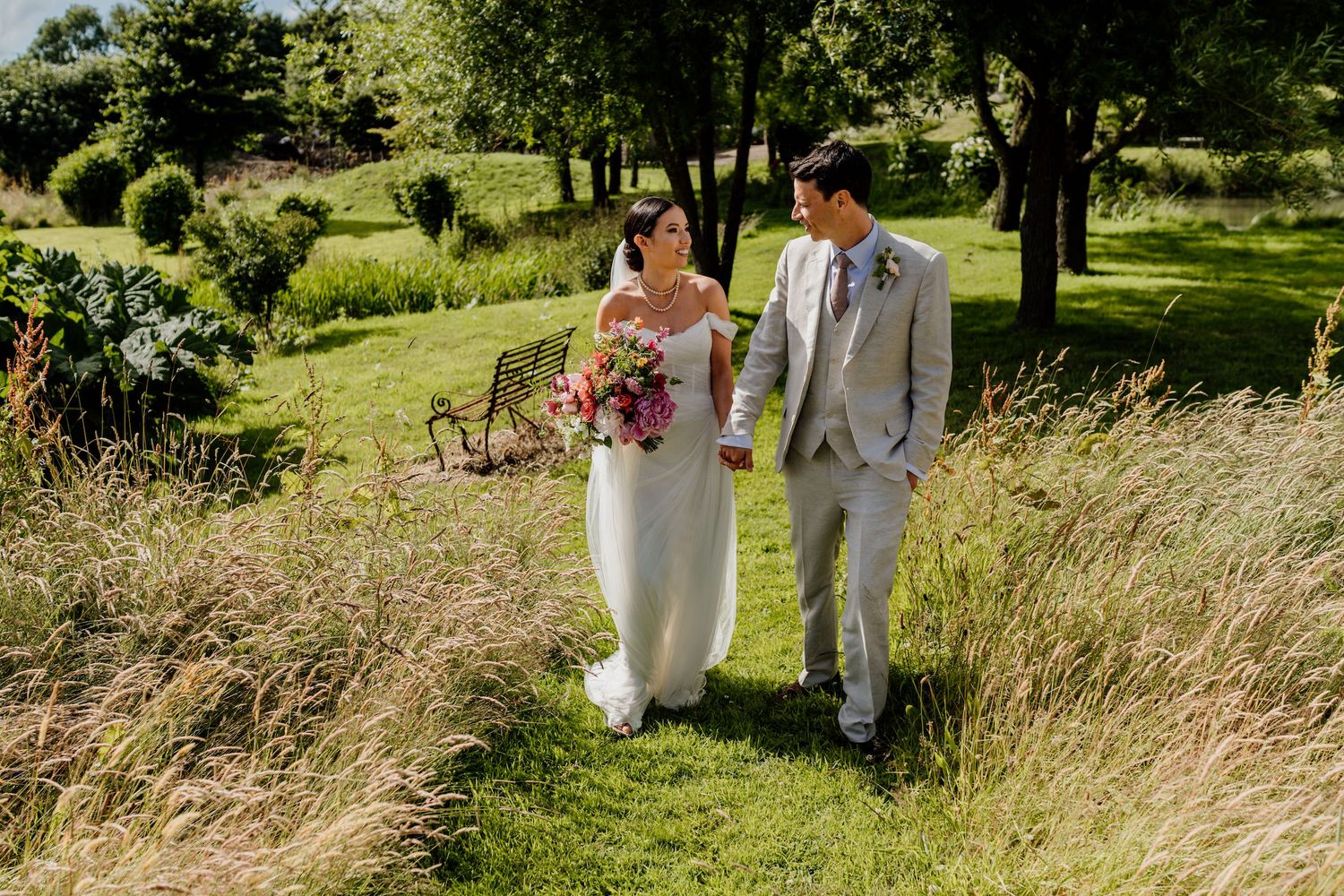 Couple walking together through tall grass on sunny wedding day.