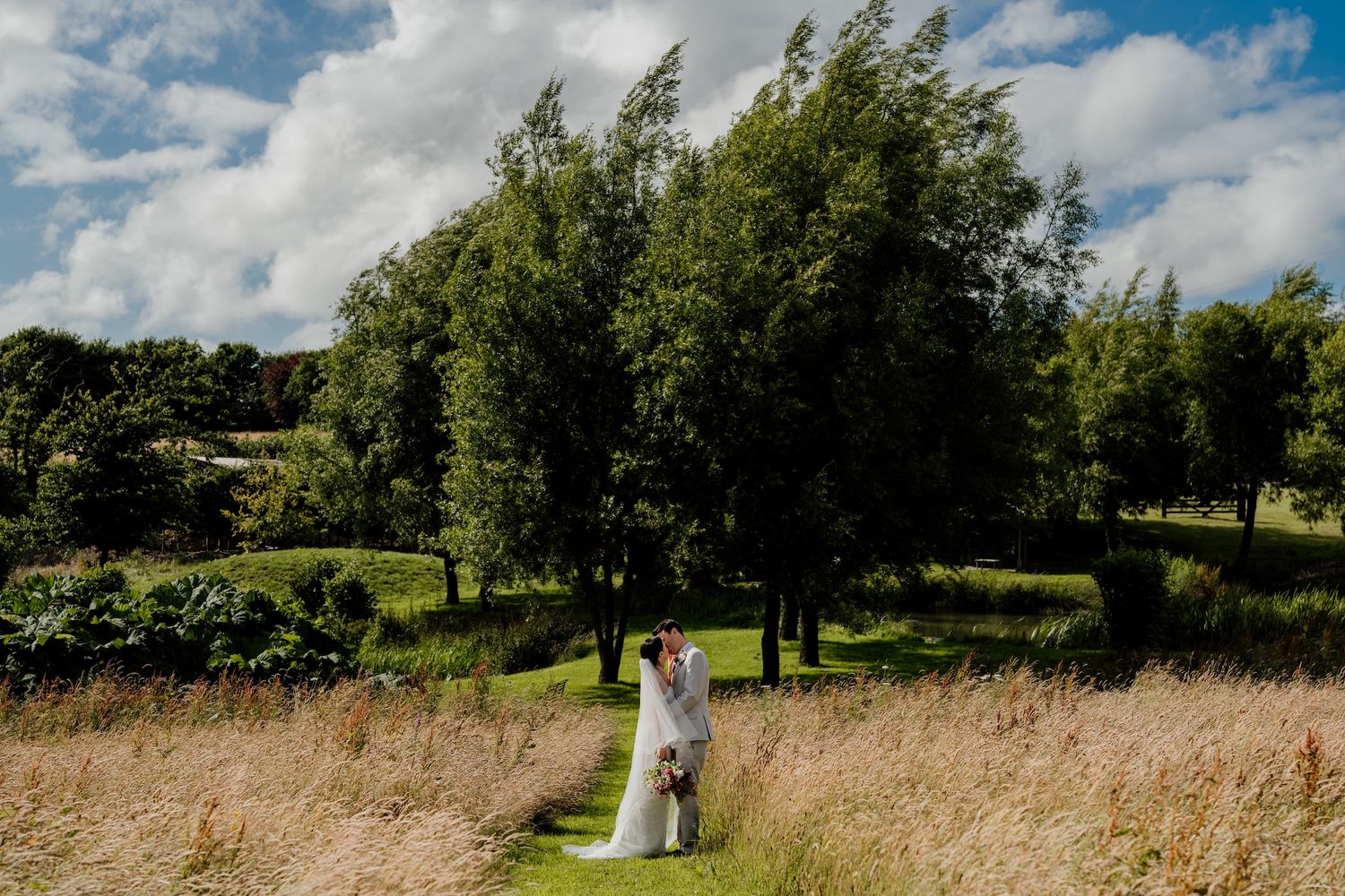 Beautiful wedding couple photographed in an open field under bright blue summer skies.