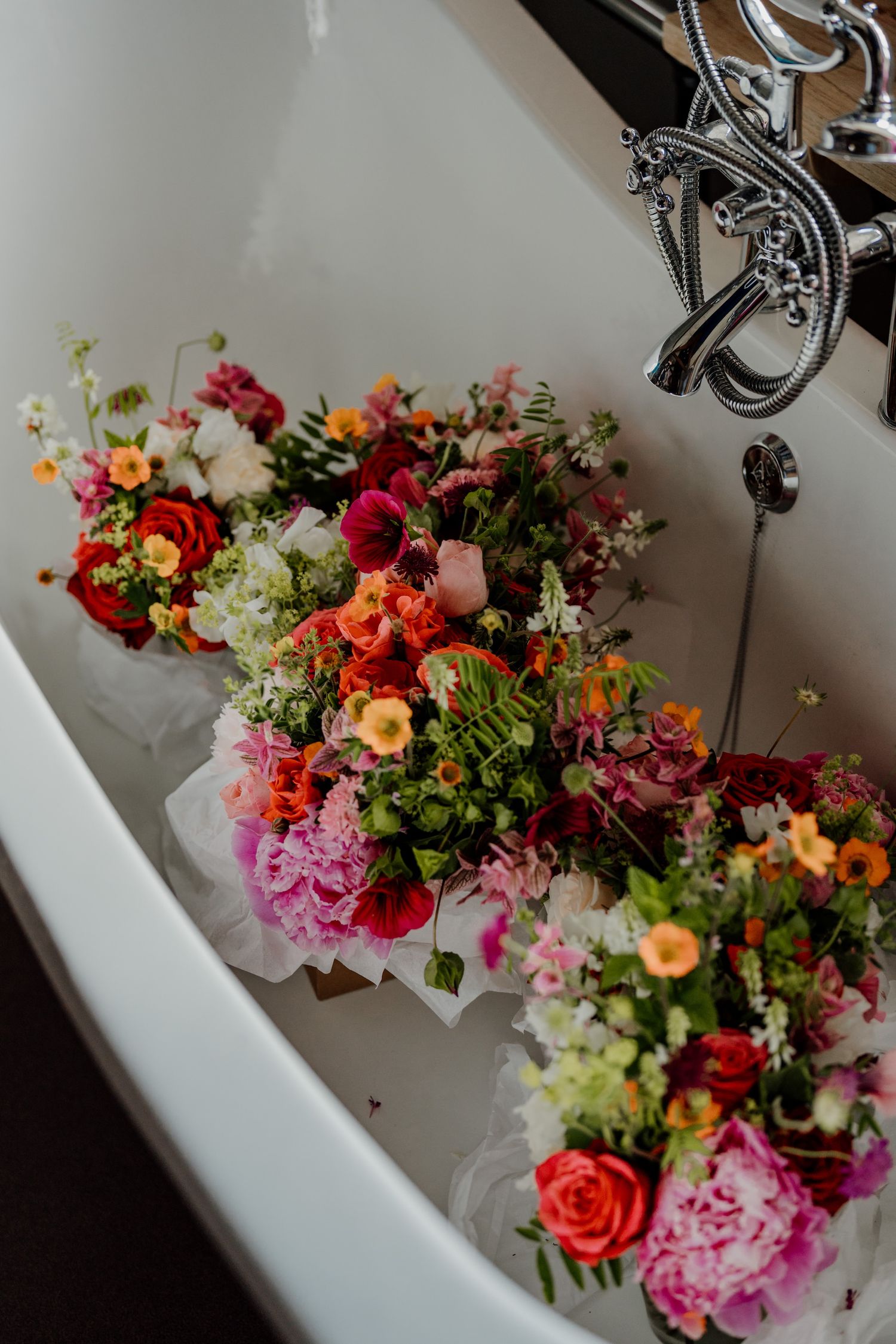 Vibrant floral arrangements with pink, orange, and red blooms displayed in white sinks.