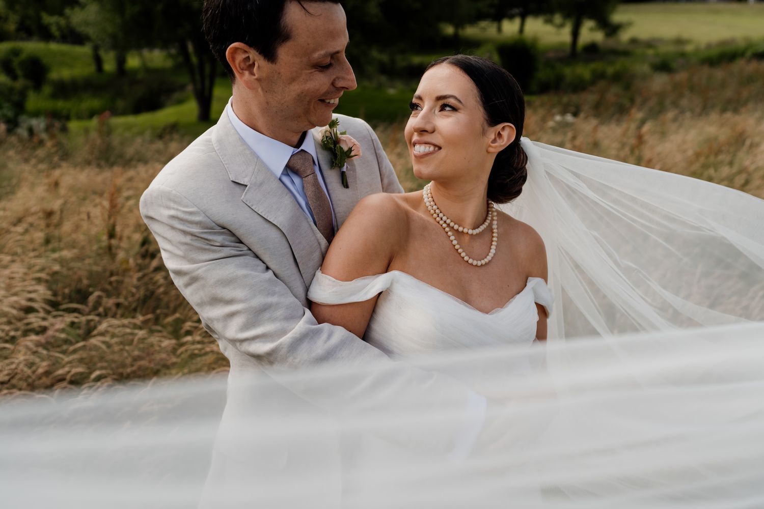 Couple shares romantic moments in a grassy field during their wedding portraits.