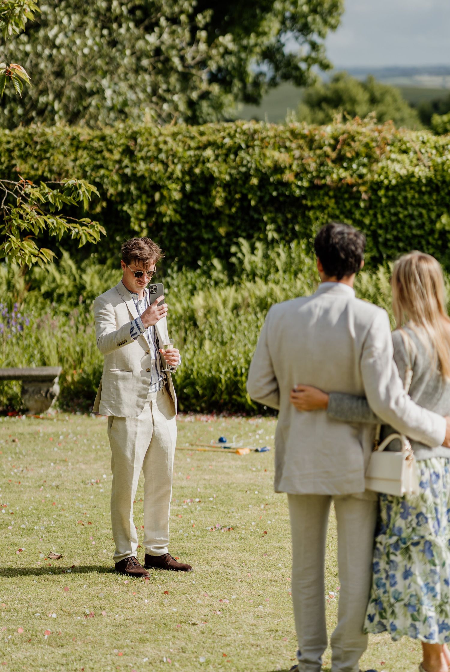 A sequence showing people in light-colored outfits socializing at an outdoor garden party on a sunny day.