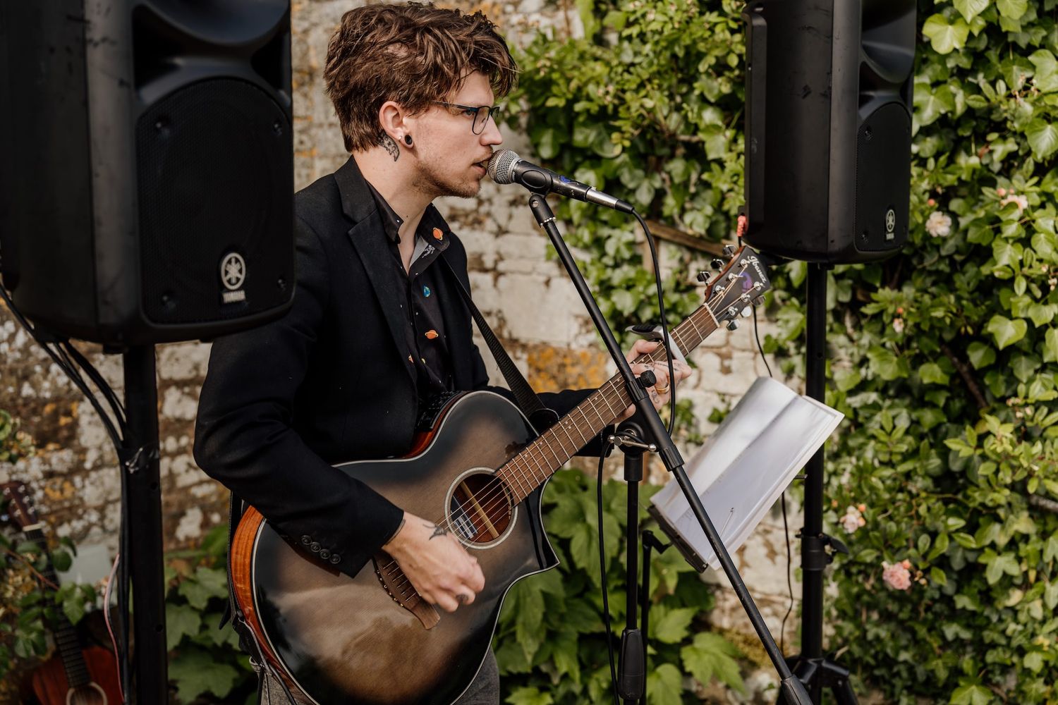 Musicians in formal attire perform together on stage with string instruments against a leafy green backdrop.
