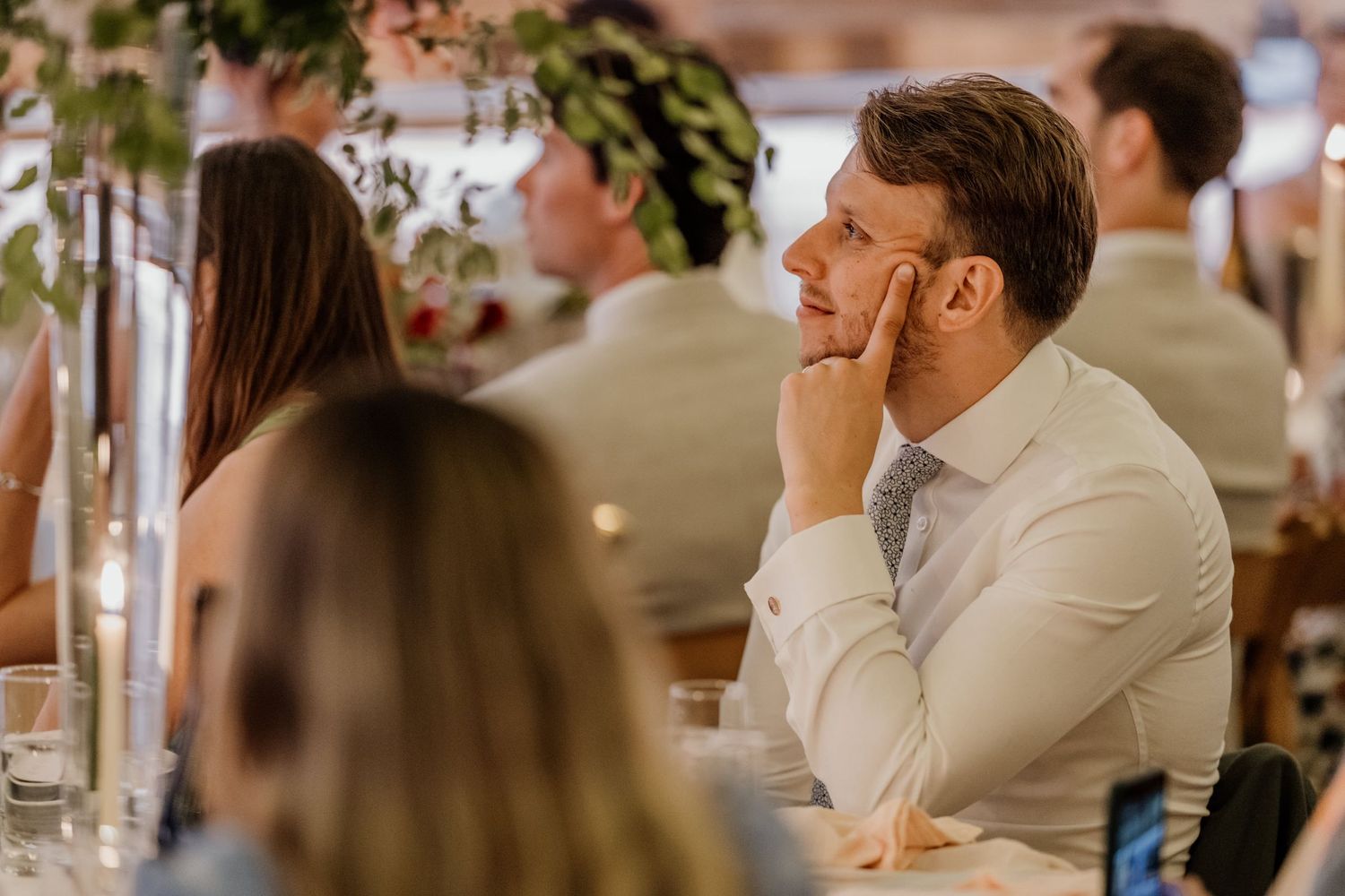 A gathering of elegantly dressed guests at a formal indoor event with tall candlestick centerpieces on tables.