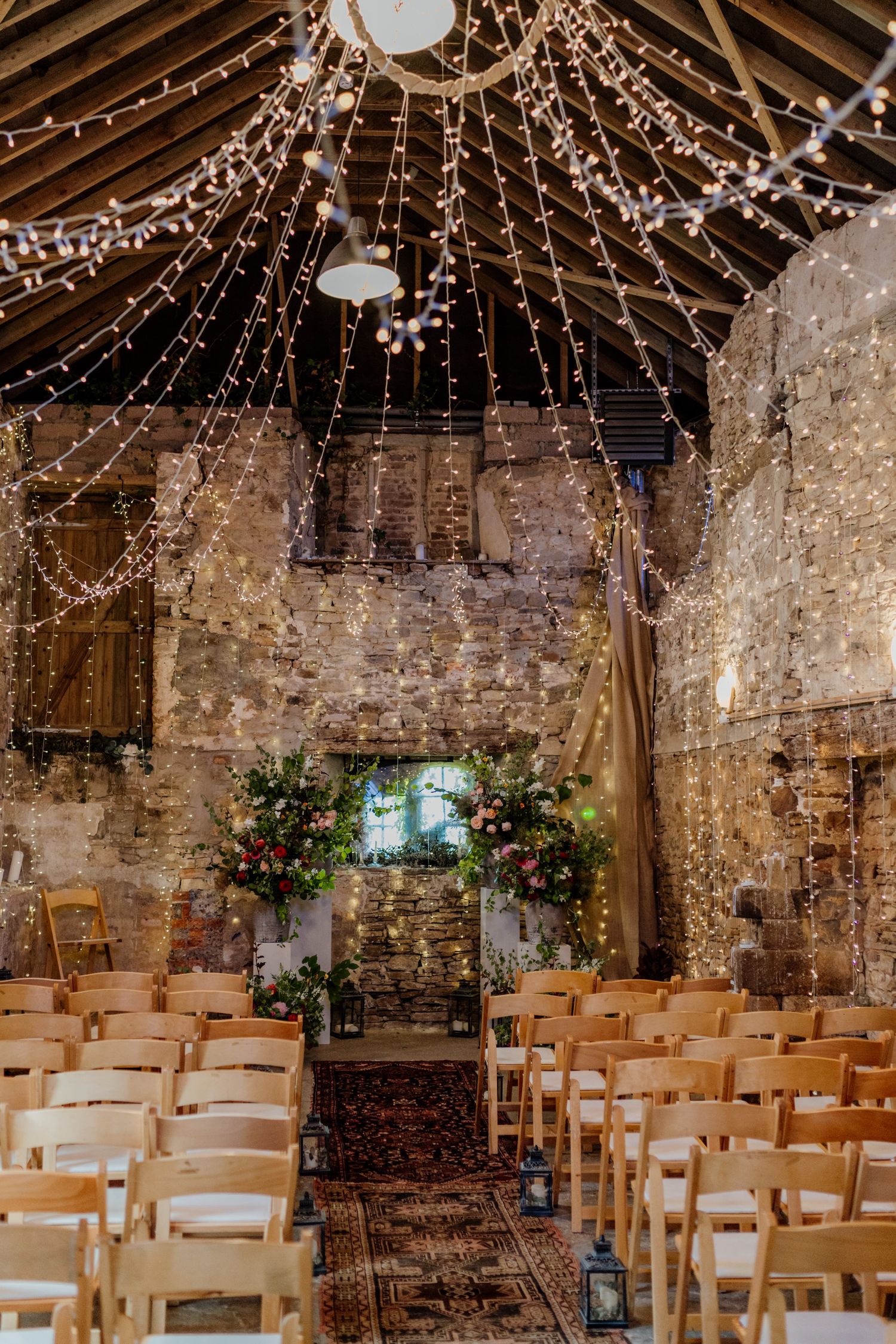 Rustic stone chapel with string lights and white chairs set up for wedding ceremony.