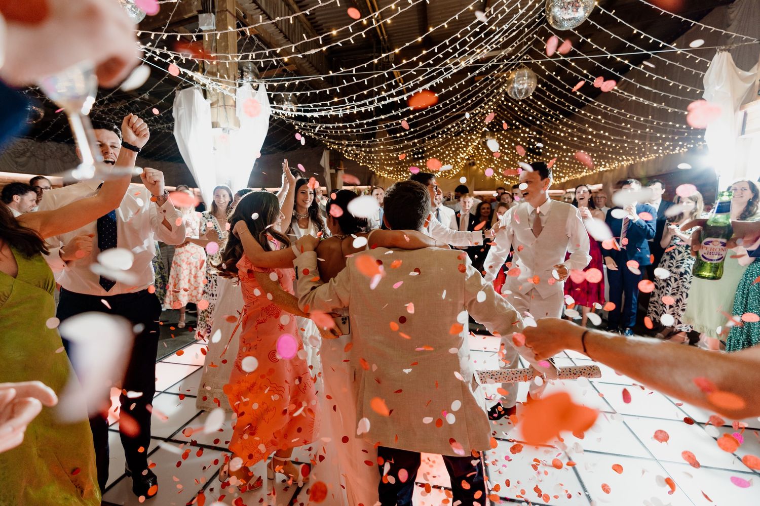 Romantic wedding celebration at dusk with fairy lights illuminating a crowd of dancing party guests.