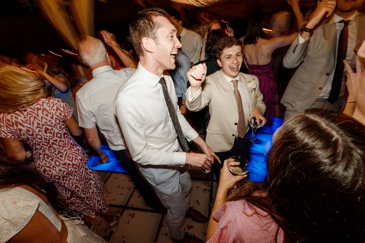 Guests dancing and celebrating at a lively wedding reception party with blue lighting effects.