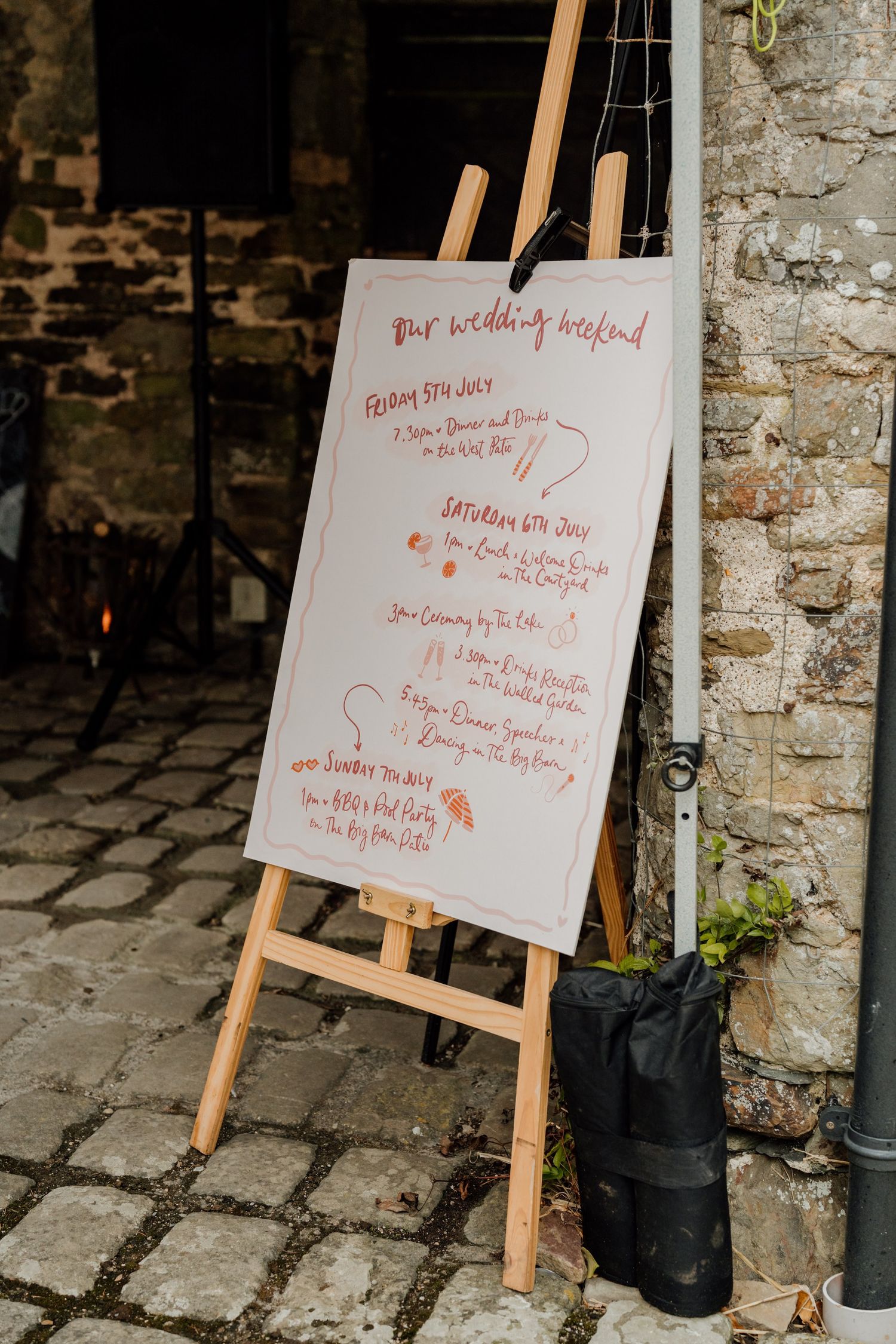 Multiple wooden easels displaying elegant wedding seating charts with calligraphy text against a rustic stone wall.