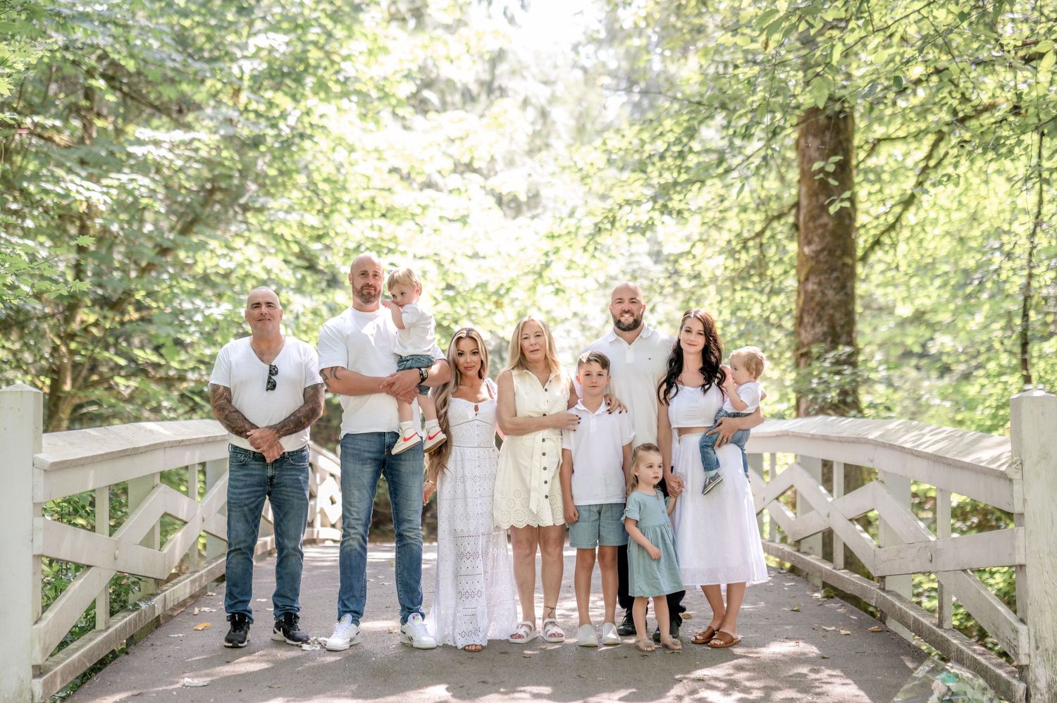 A group wearing white clothing poses together on a rustic wooden bridge in a lush forest setting.