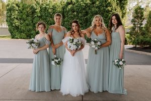 Bridal party in pale blue dresses holding white bouquets pose together outside.