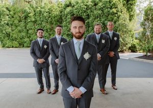 Groomsmen in gray suits lined up for formal wedding photos on outdoor porch.