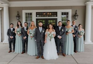 Panoramic wedding party photo with bridesmaids in light blue dresses and groomsmen in gray suits.