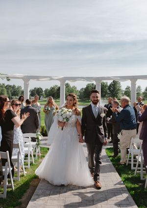 Outdoor wedding ceremony with white chairs and floral arrangements under white pergola.