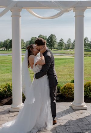Wedding couple sharing a romantic moment under a white columned pergola overlooking a golf course.