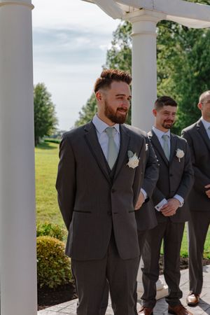 Groomsmen in dark suits line up along a white columned porch during wedding celebrations.