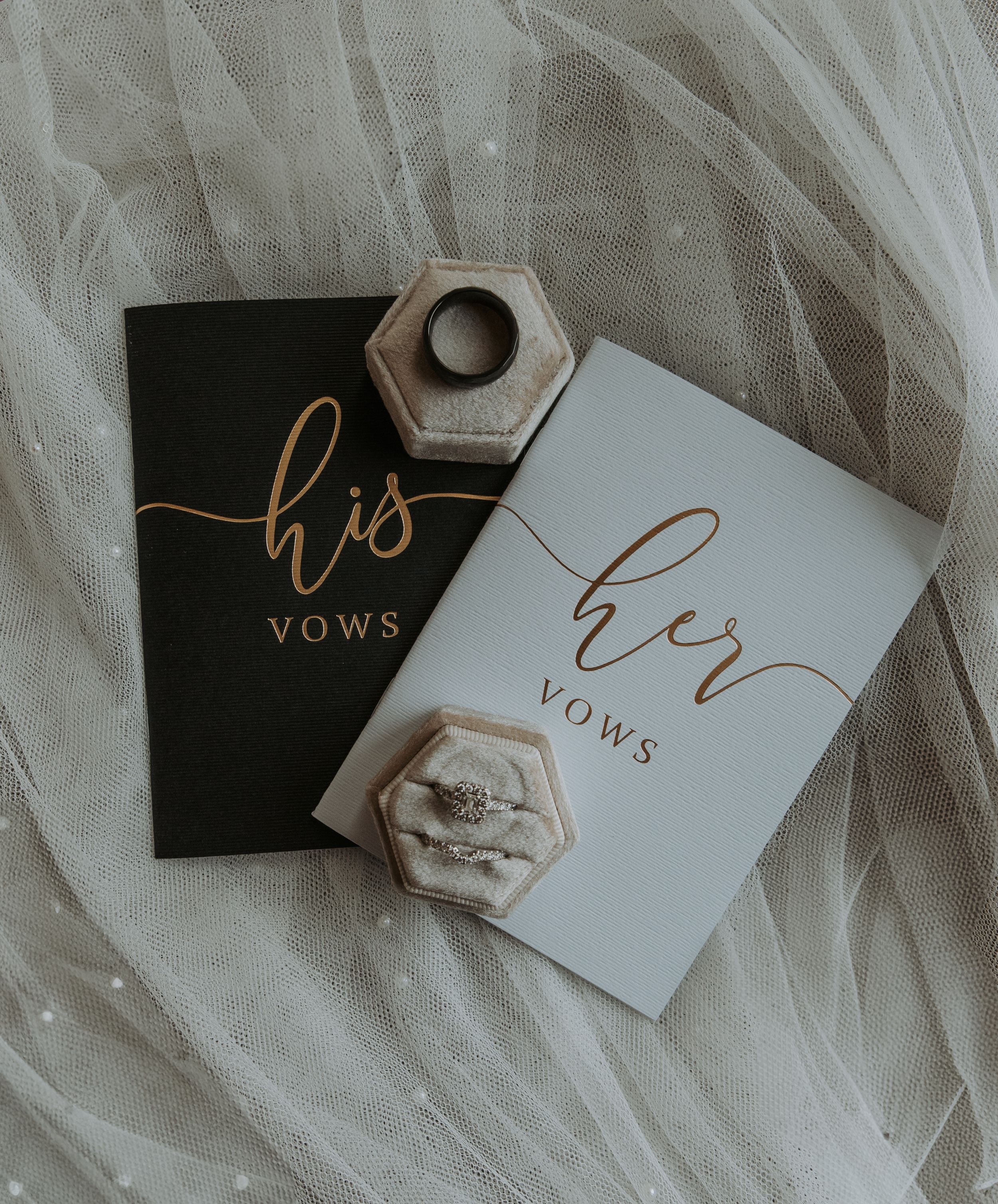 Elegant wedding vow books and ring boxes on white tulle fabric.