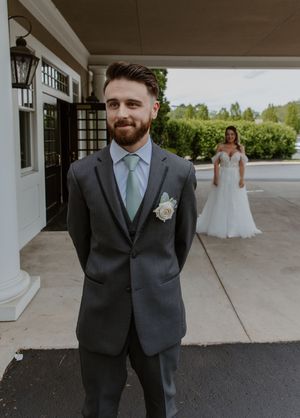 Wedding party dressed in gray suits and gowns standing outside a columned building.