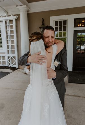Emotional first look between wedding couple sharing an intimate embrace outside a white columned venue.