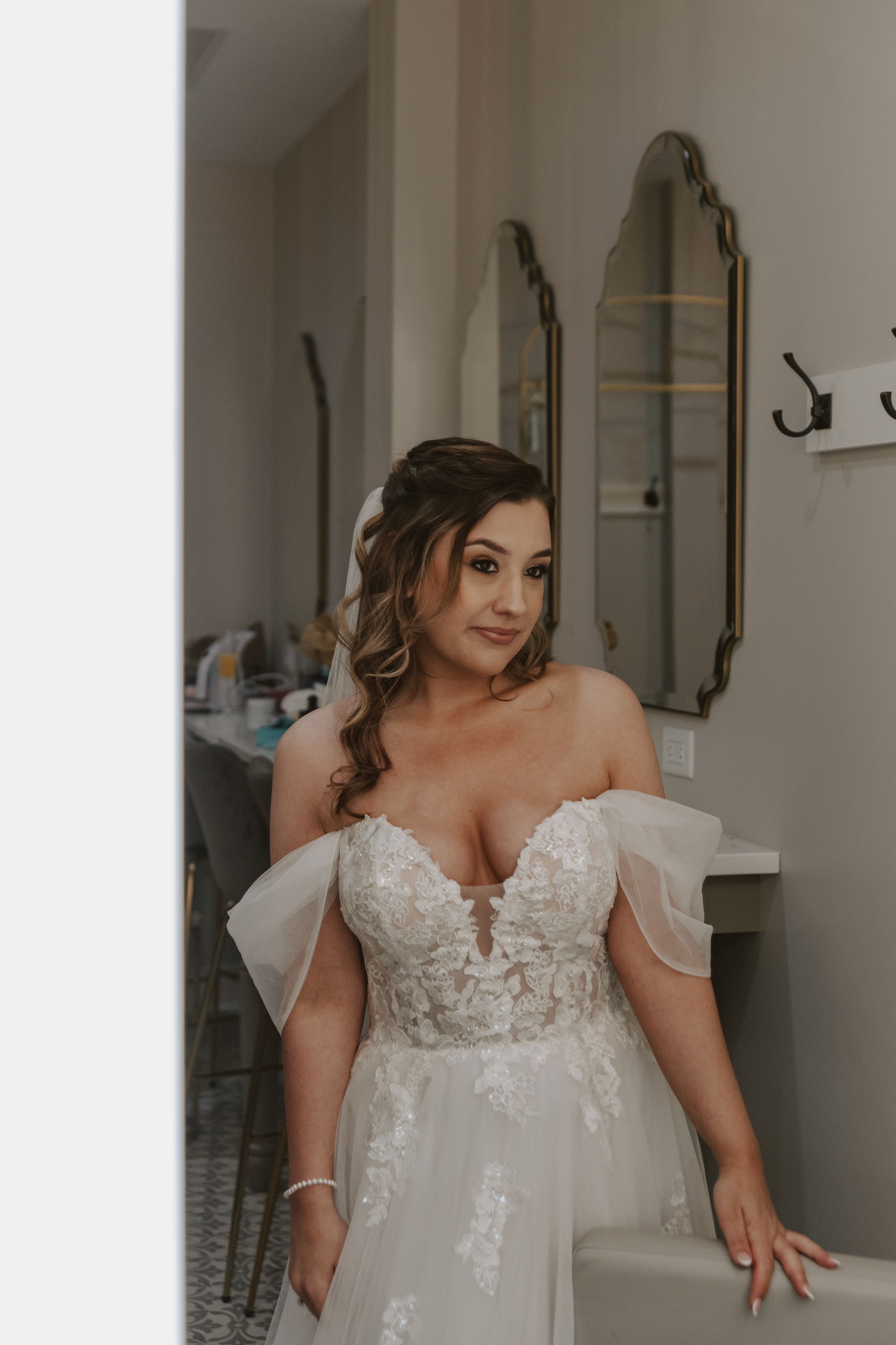 A beautiful white lace wedding dress with off-shoulder details shown in a getting ready room.
