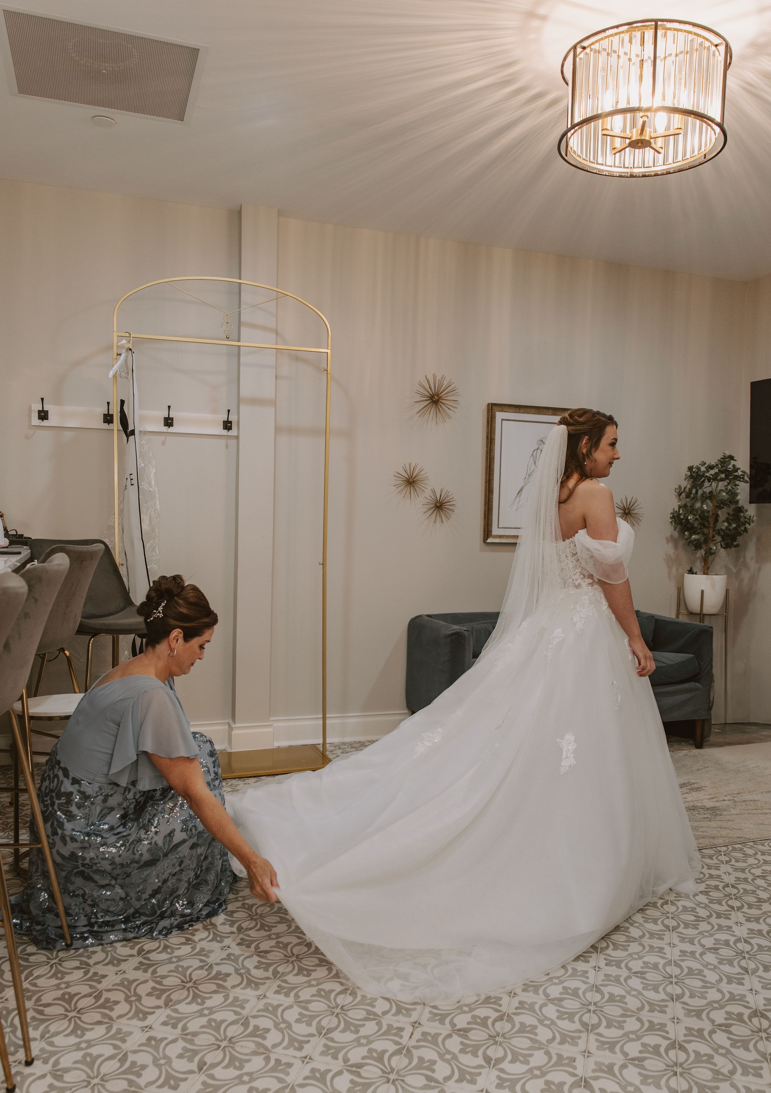 Wedding dress in motion as photographer captures flowing train on patterned floor in bright sunlit room.