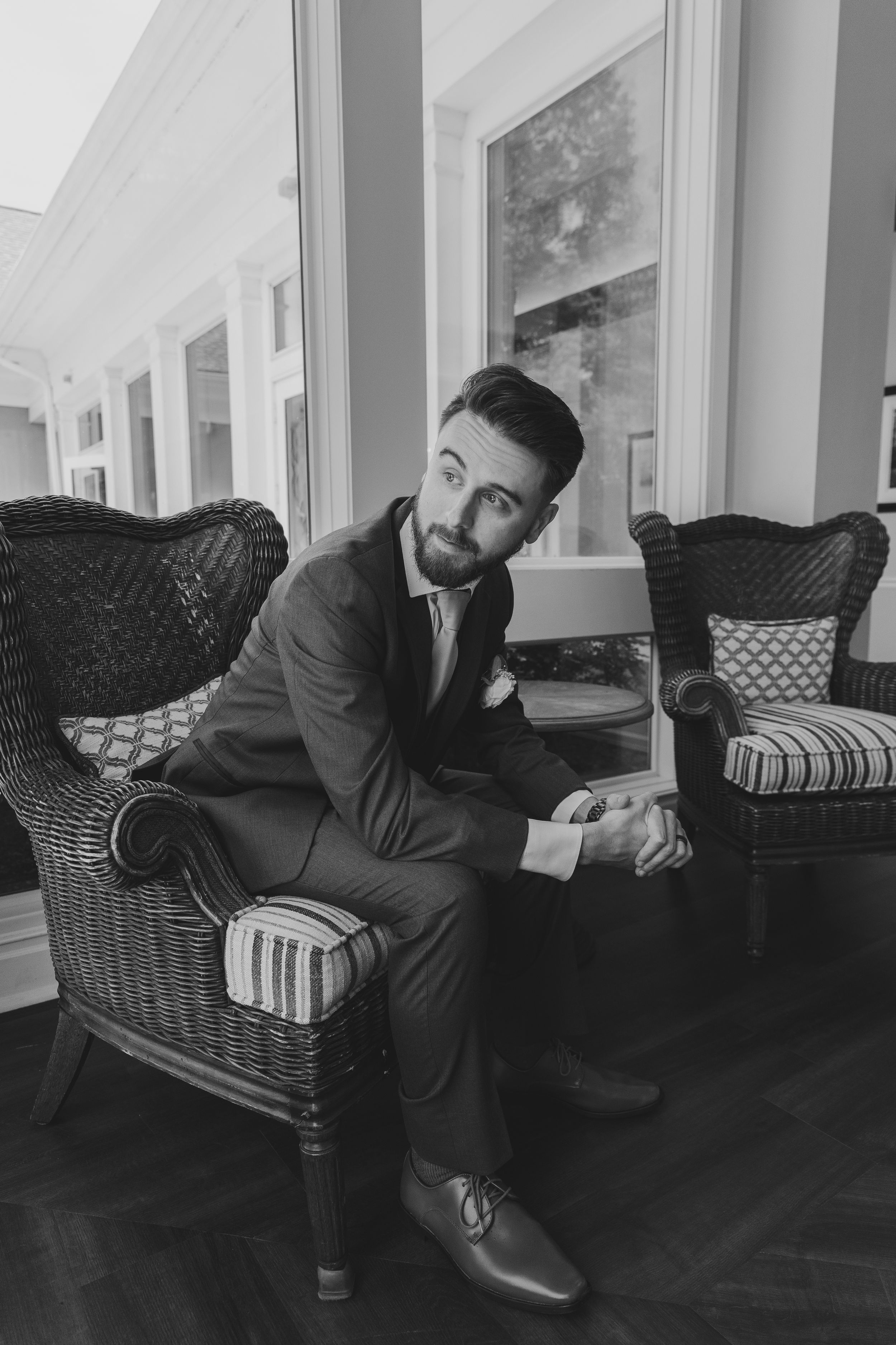 Artistic black and white series showing seated person in formal wear lounging on a wicker couch.