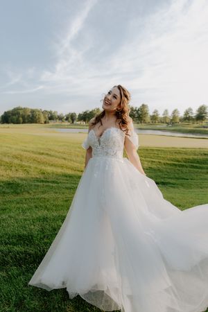 Flowing white wedding dress twirls against a sunlit grassy field during golden hour.