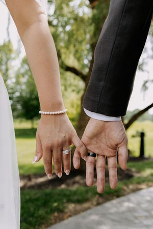 Close-up of wedding couple's hands displaying their rings against a white railing outdoors.