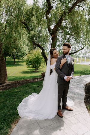 First look moment captured in a garden setting with willow trees and a white stone pathway.
